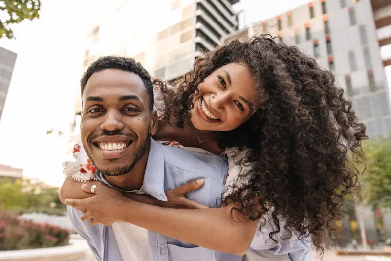 Smiling man carrying a smiling woman piggy back.TEXT